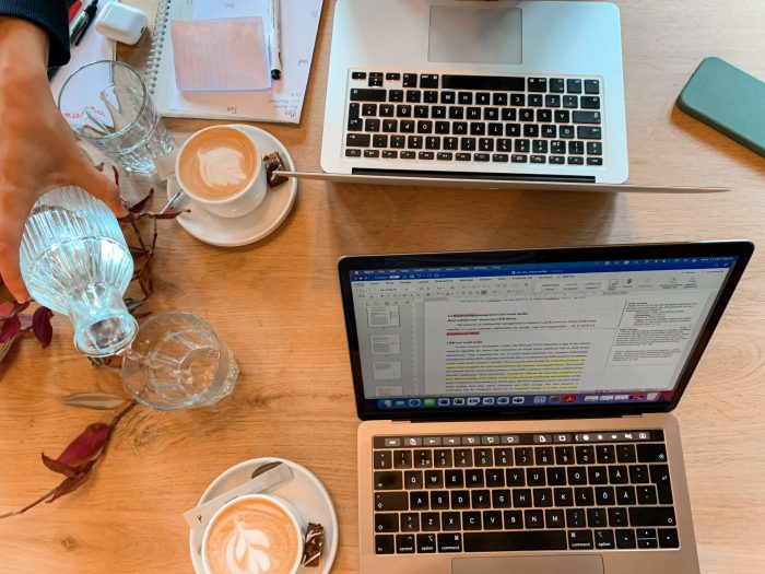 Två studenter med datorer och kaffekoppar på ett cafe