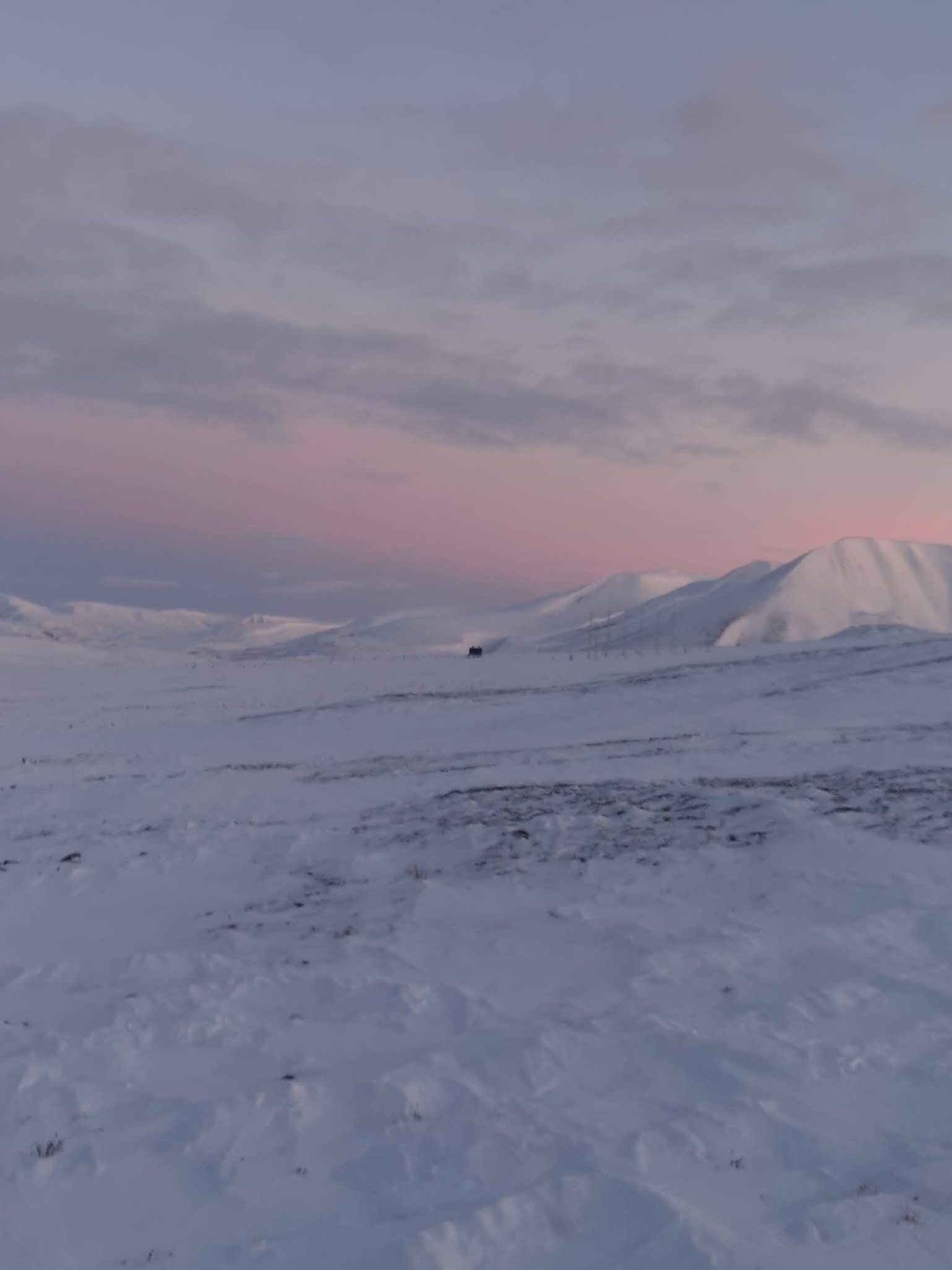 Ett snötäckt landskap med rosa och orange toner som syns genom hela bilden. Berg och glaciärer syns i bakgrunden.  