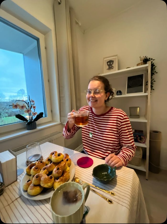 Kvinna som dricker te och har lussebullar framför sig.