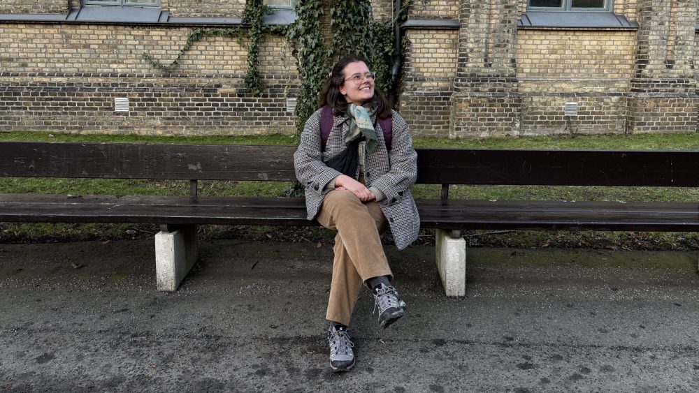 Tjej sitter på bänk och tittar snett upp mot himmelen