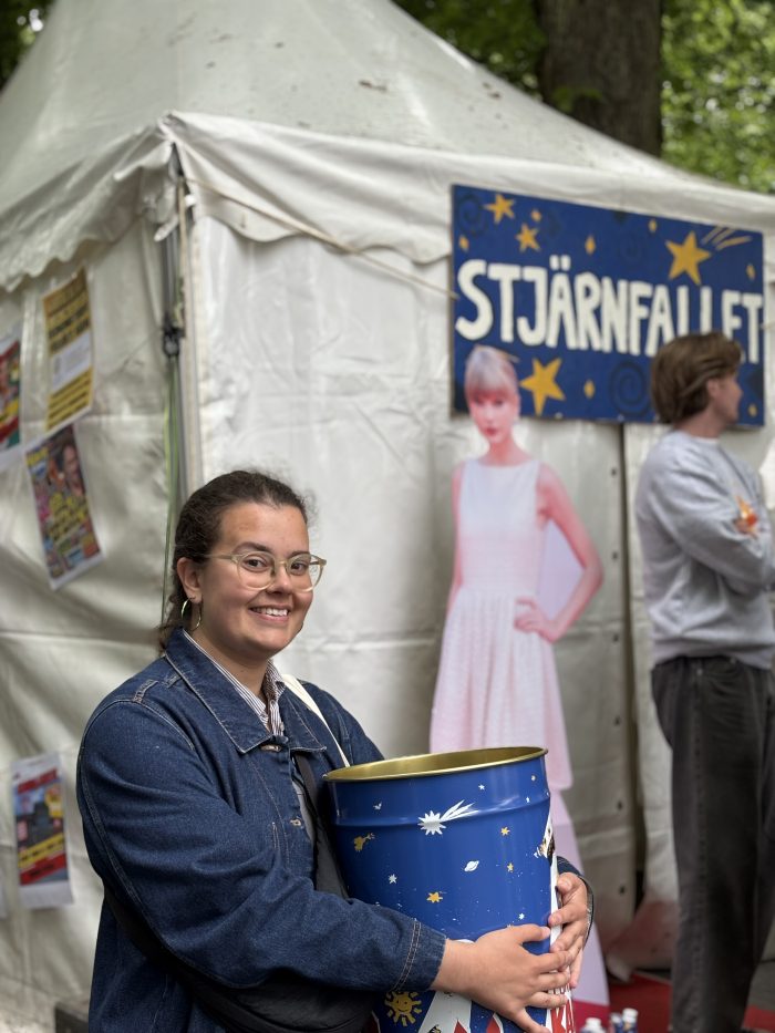Nicole står och håller sin karnevalssopptunna framför en Taylor Swift-kartong.
